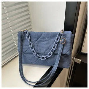 Detail of blue denim envelope bag featuring diamond quilting and stylish chain strap