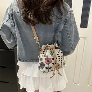 Borsa a secchiello floreale boho con coulisse in pelle indossata da modella in denim