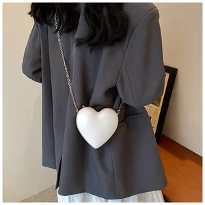 Mini white heart-shaped chain bag with pearl luster finish shown on a model