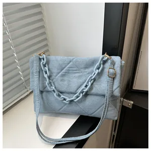 Detail of light blue denim envelope bag with quilted diamond pattern and chunky chain