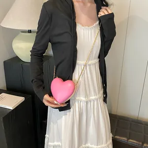 Pink heart-shaped crossbody bag with gold chain strap shown on a model's outfit