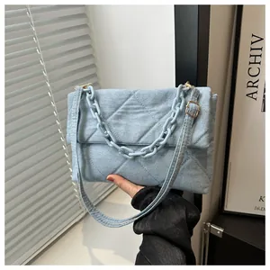 Close-up of light blue denim envelope bag with quilted patterns and chunky plastic chain