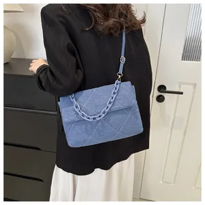 Detail of blue denim envelope bag with white quilted stitching and chunky plastic chain