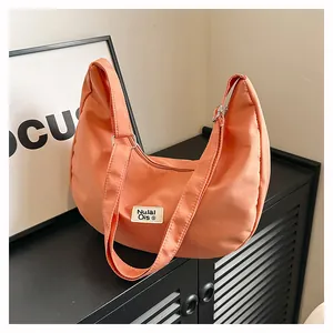 Detail of a coral nylon hobo bag with adjustable strap and logo tag on a textured stand