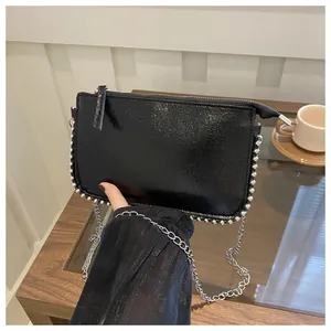 Detail der glänzenden schwarzen Lackledertasche mit Silbernieten und Kette