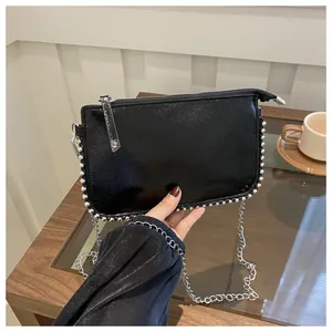 Detail einer schwarzen Lackleder-Umschlagtasche mit silbernen Nieten und Kette