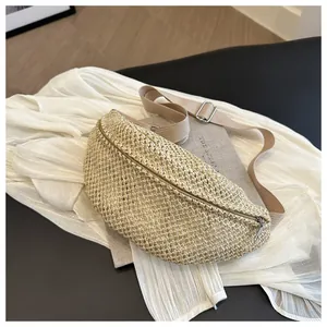 Detailed close-up of woven straw crescent waist bag with silver zipper and fabric strap