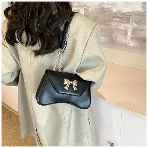 Detail of black crossbody bag with silver bow buckle and chain strap on a blazer