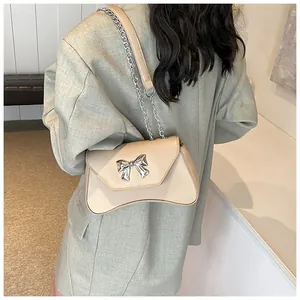 Detail of beige faux leather shoulder bag with silver bow accent and curved bottom base