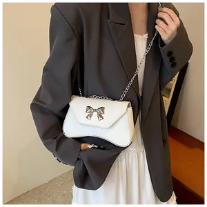 Detailed view of white faux leather crossbody bag with a gold metal bow and chain strap