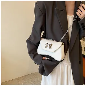 Detail of white leather crossbody bag featuring a silver bow accent and chain strap