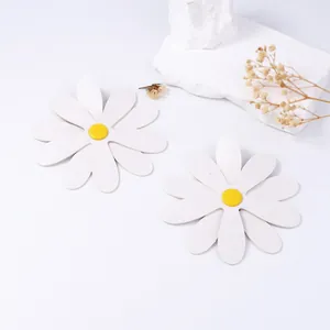 Macro detail of white PU leather daisy earrings on a minimalist decorative stone