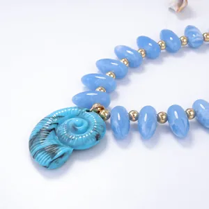 Détail macro des perles bleues et du pendentif conque sur un collier style océan