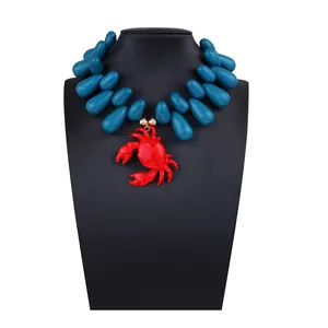 Dettaglio collana con perline blu a goccia e pendente a granchio rosso su espositore nero