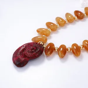 Détail macro du pendentif nautile rouge et collier de perles ambre avec accents dorés