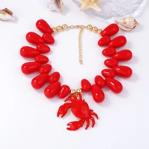 Dettaglio ravvicinato di perle rosse a goccia e ciondolo a granchio su collana dorata