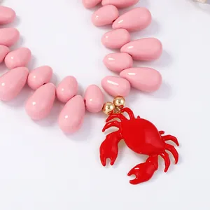 Dettaglio collana di perle rosa con ciondolo a forma di granchio rosso e finiture oro