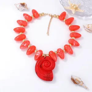 Détail du collier à perles orange avec un grand pendentif en forme de coquillage rouge