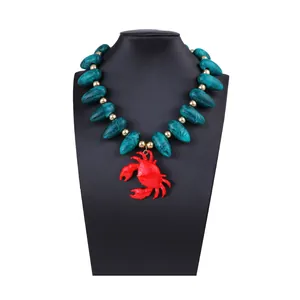 Gros plan des perles marbrées vertes et du grand pendentif crabe rouge sur le collier