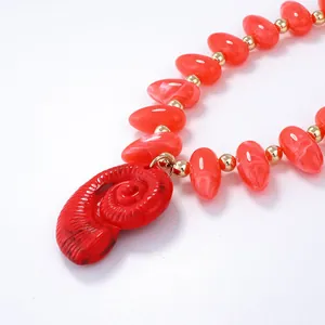 Gros plan du pendentif nautile rouge avec perles marbrées et accents dorés sur fond blanc