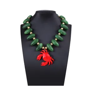 Gros plan du pendentif crabe rouge et des perles vertes texturées du collier