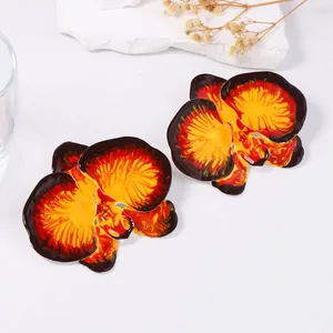 Macro detail of orchid floral earrings with vivid orange enamel petals and yellow core