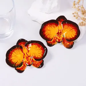 Macro detail of vibrant orchid earrings with red orange enamel and glossy finish
