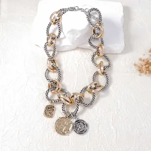 Détail d'un collier chaîne bicolore avec pendentifs de pièces vintage et maillons texturés