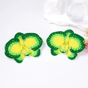 Macro detail of orchid-shaped yellow and green gradient floral earrings on white marble