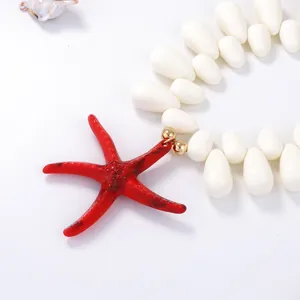 Detail of red starfish pendant on cream beaded necklace with golden sphere accents