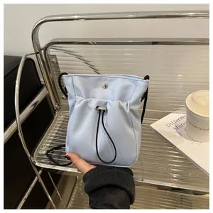 Detailopname van lichtblauwe nylon schoudertas met zwart trekkoord en metalen drukknoopsluiting