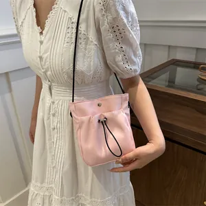 Mini roze nylon crossbodytas met trekkoord, gedragen door een model in het wit