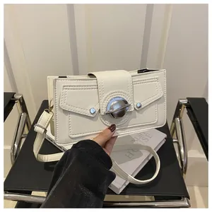 Détail d'un sac bandoulière blanc en cuir avec boucle planète argentée sur un livre