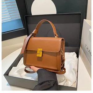 Detail of a brown leather handbag featuring a golden geometric lock and top handle