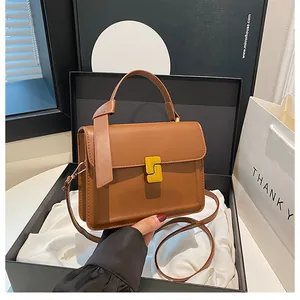 Detail of a brown leather handbag with a gold geometric lock in a luxury gift box