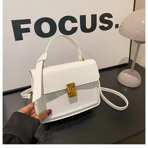 Detail of white leather handbag with gold L-shaped buckle and wrapped handle on desk