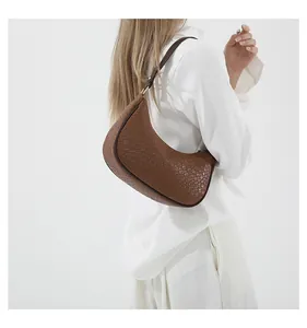 Detail of a brown woven crescent crossbody bag worn by a model on a white background