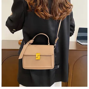 Detail of khaki square handbag with golden geometric clasp on a black blazer background
