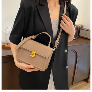 Detail of khaki square handbag with gold buckle held by a model in a modern room