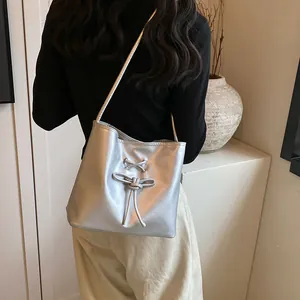 Silver metallic ballet-style bucket bag with bow detail shown in a minimalist setting