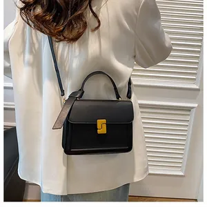 Detail of a minimalist black square handbag with gold buckle and leather texture