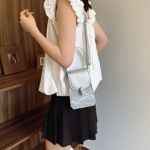 Minimalist silver crossbody phone bag with pleated texture and metal buckle on a model