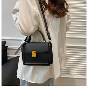 Detail of elegant black square handbag with golden geometric clasp and top handle
