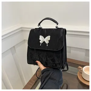 Detail of black pleated crossbody bag featuring a silver metal butterfly ornament