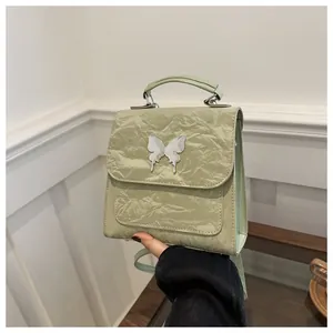 Detail of mint green textured leather backpack with a silver metal butterfly ornament