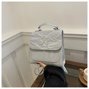 Detail view of silver mini backpack with wrinkled texture and metal butterfly ornament