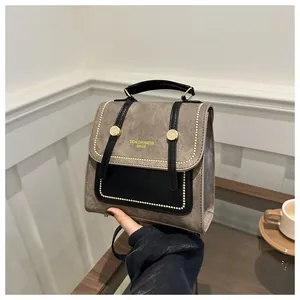 Détail d'un mini sac à dos bicolore avec rivets dorés et poignée sur une table en bois
