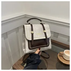 Détail d'un sac à dos en cuir gris et marron avec ferrures dorées dans un café urbain