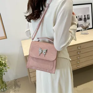 Pink crossbody bag with butterfly buckle shown on model in a cozy interior setting
