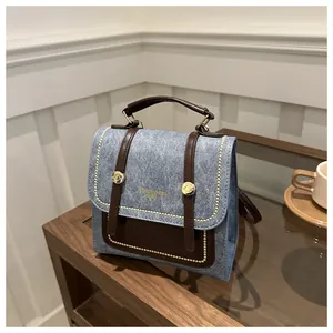 Détail du sac rétro en denim bleu et cuir marron avec rivets dorés sur table en bois